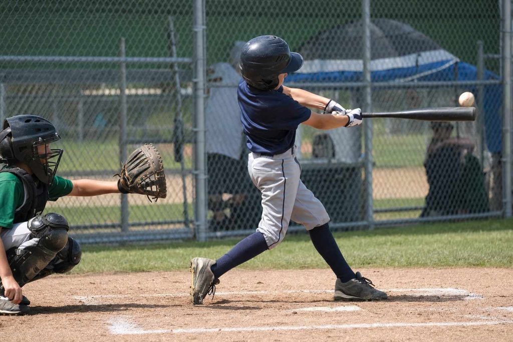 A youth baseball batter mid-swing at home plate on a sunny field