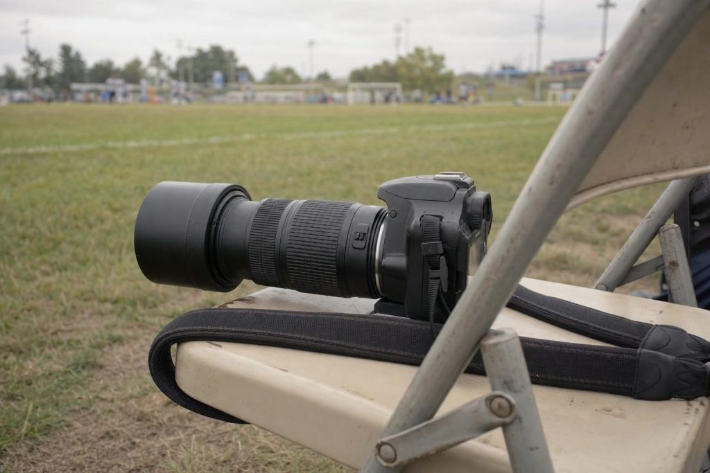 An entry-level camera with a telephoto lens at the edge of a sports field
