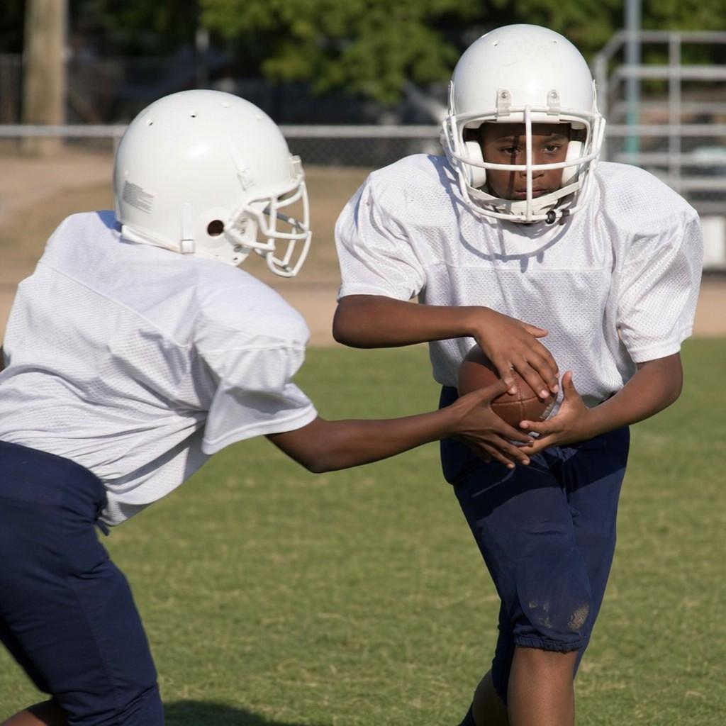 A youth football handoff in daylight