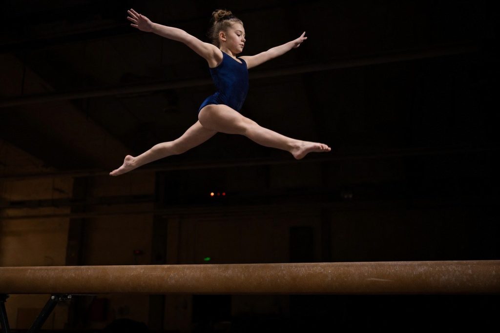 A youth gymnast at the peak of a leap on a balance beam