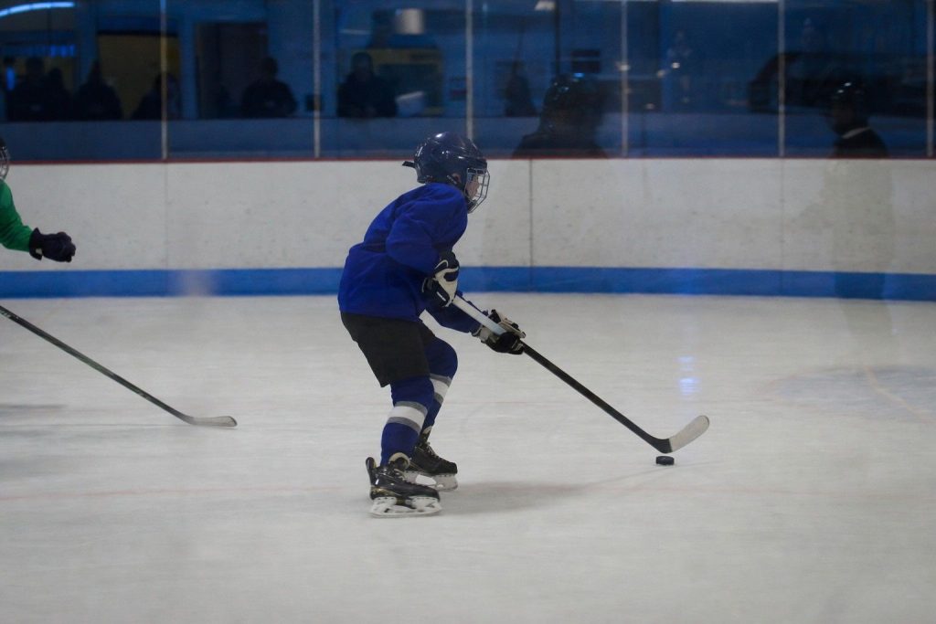 A youth hockey player skating with the puck in a dim rink