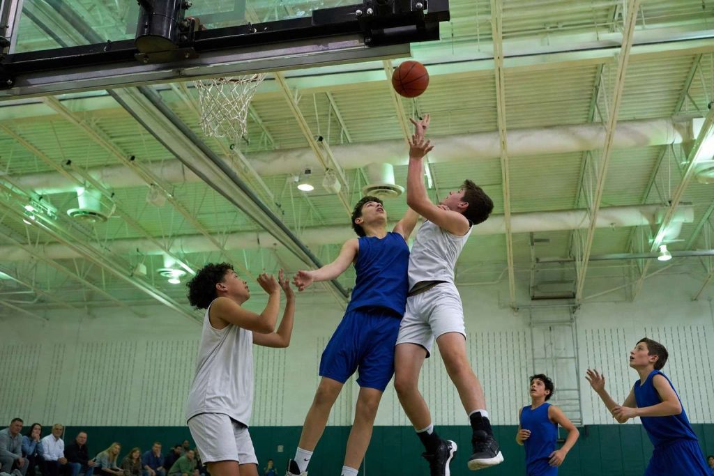 Youth basketball players leaping for a rebound in a dim school gym