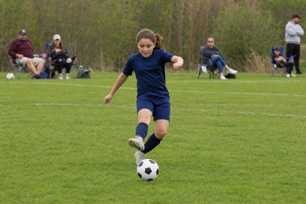 Youth soccer player running and kicking the ball toward the camera on a grass field